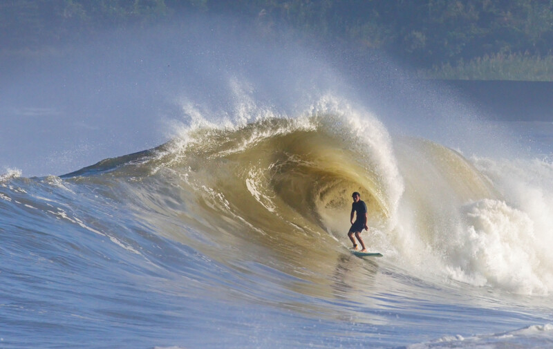 Surfer riding inside a large barrel wave with spray exploding over the crest.
