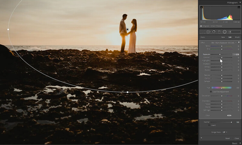Two people standing on rocky terrain silhouetted against golden sunset light over water.