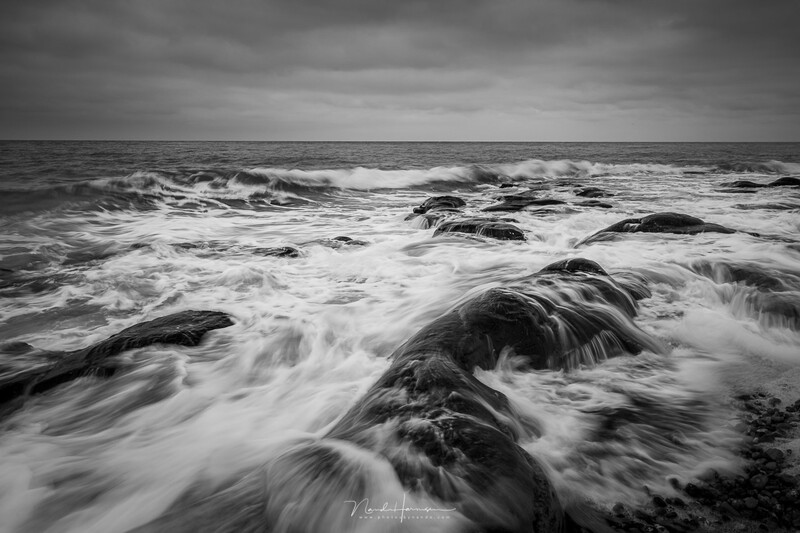 Seascape with waves cascading over dark rocks under stormy sky, shot with long exposure.