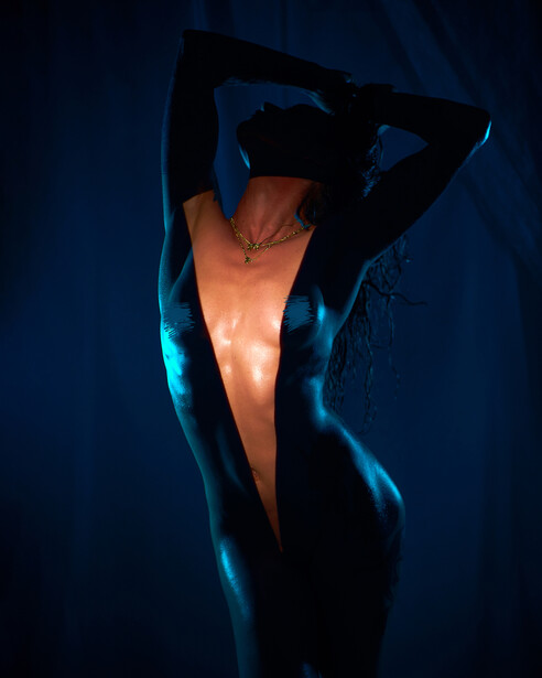 Silhouetted figure with arms raised against glowing blue and orange lighting in dark studio setting.