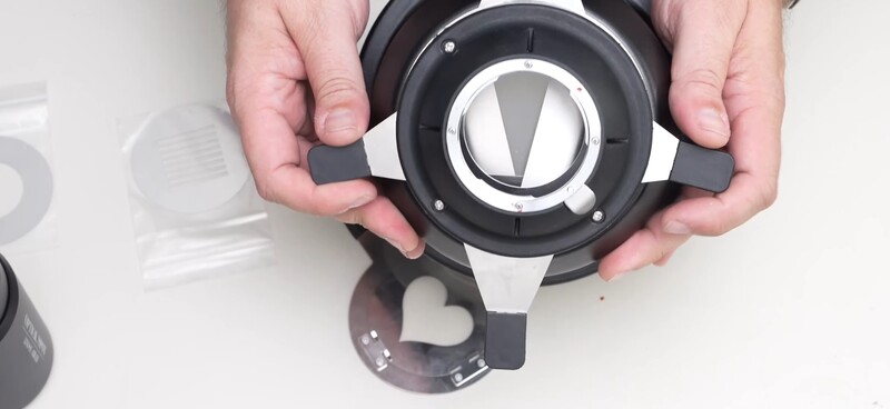 Hands holding a disassembled camera lens mount showing internal mechanical components and optical elements.