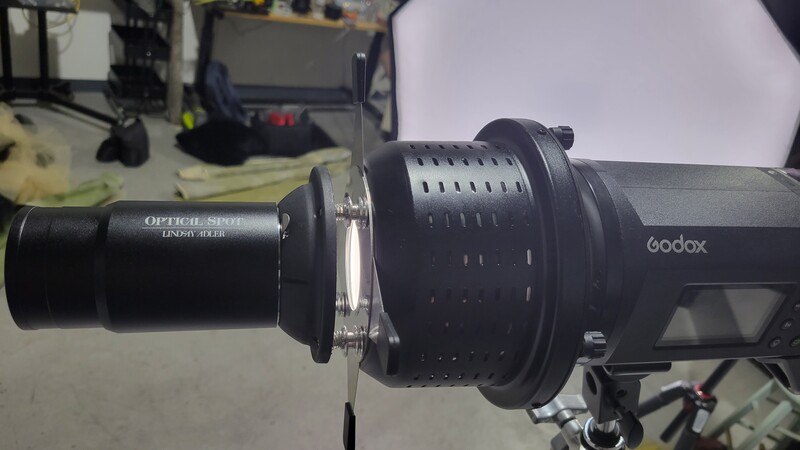 Godox monolight with optical slave trigger and modifier attachment on studio workbench.
