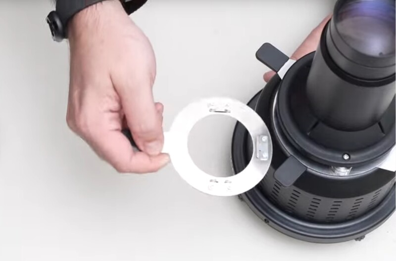 Person's hand holding a white lens adapter ring next to a telephoto lens with visible glass elements.