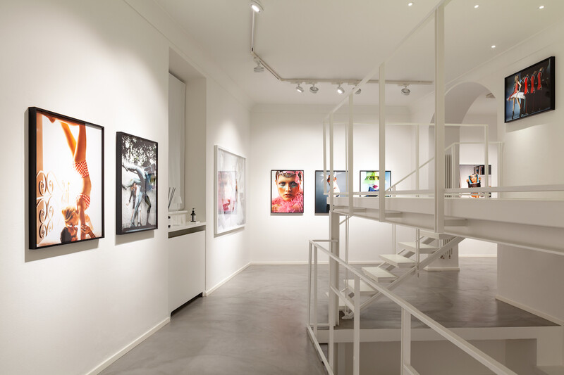Modern gallery interior with framed artworks displayed on white walls and glass partitions.