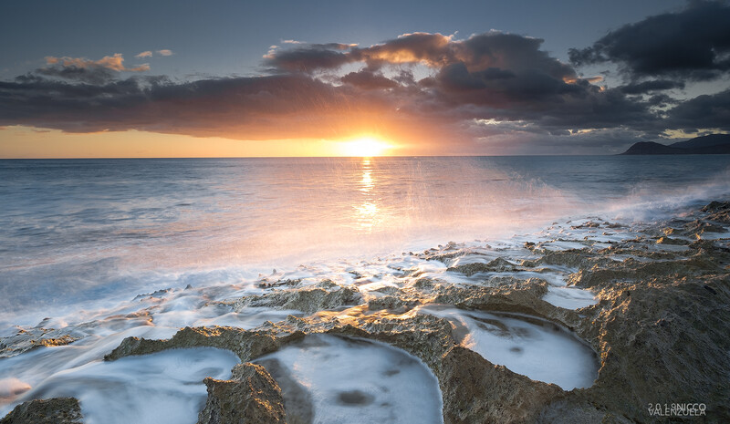 Rocky shoreline with tide pools at sunset, golden light reflecting across calm ocean water.