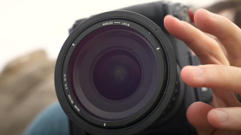 Close-up of a telephoto zoom lens held in hand, showing the barrel markings and front element against an outdoor background.