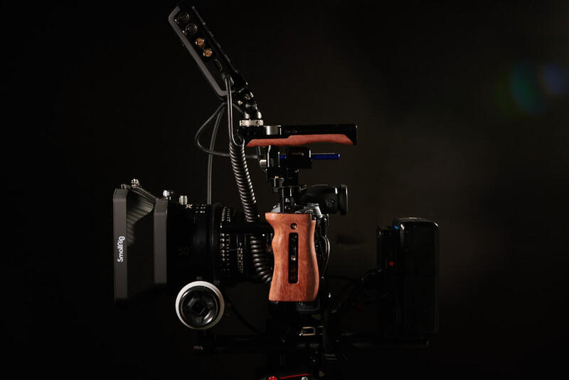 Professional cinema camera rig with wooden handgrip, follow focus system, and mounted microphone on black background.