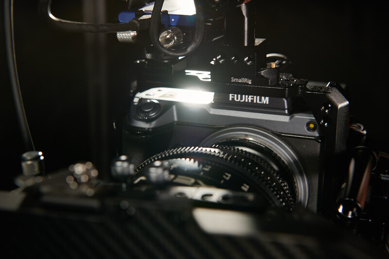 Fujifilm camera with cinema lens mounted on a black surface under studio lighting.