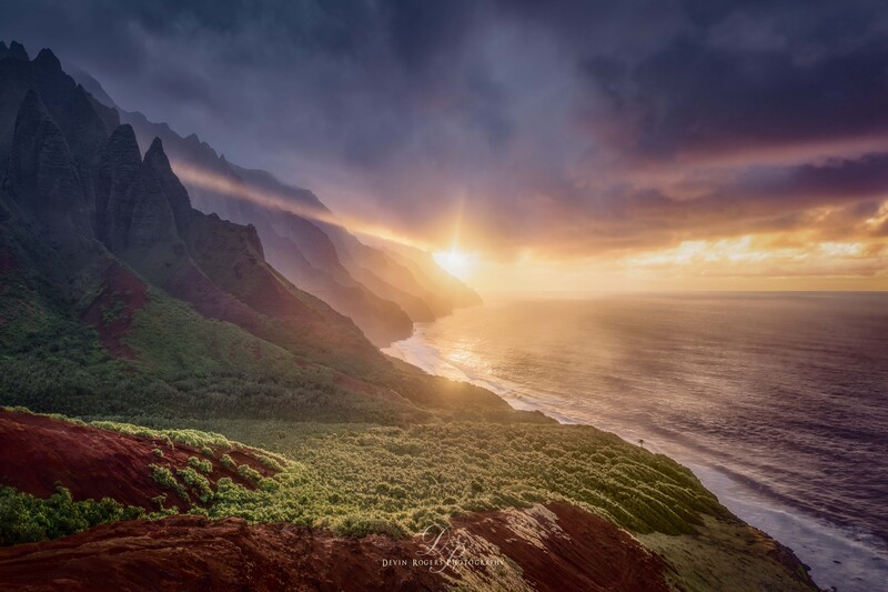 Dramatic sunset over a rugged coastal mountainside with golden light breaking through storm clouds above the ocean.