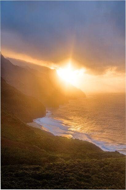 Golden sunrise illuminates coastal cliffs and beach below, with warm light breaking through clouds over the ocean.