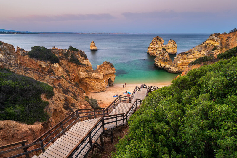 Wooden boardwalk descending to a secluded beach cove bordered by golden rock formations and turquoise water.