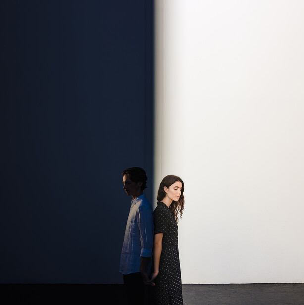 Two women standing against a minimalist backdrop with sharp geometric division between dark blue and white sections.