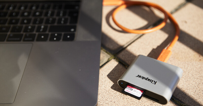 Kingma portable card reader with SD card next to laptop keyboard on textured surface.