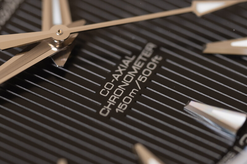 Close-up of eyeglasses resting on a dark striped surface with embossed text visible beneath the frames.