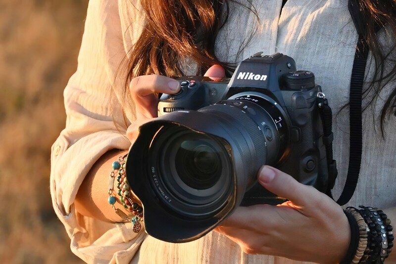 Photographer holding a Nikon DSLR camera with telephoto lens in golden hour sunlight.