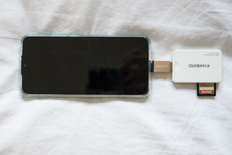 Smartphone with card reader adapter and memory card laid out on white fabric.