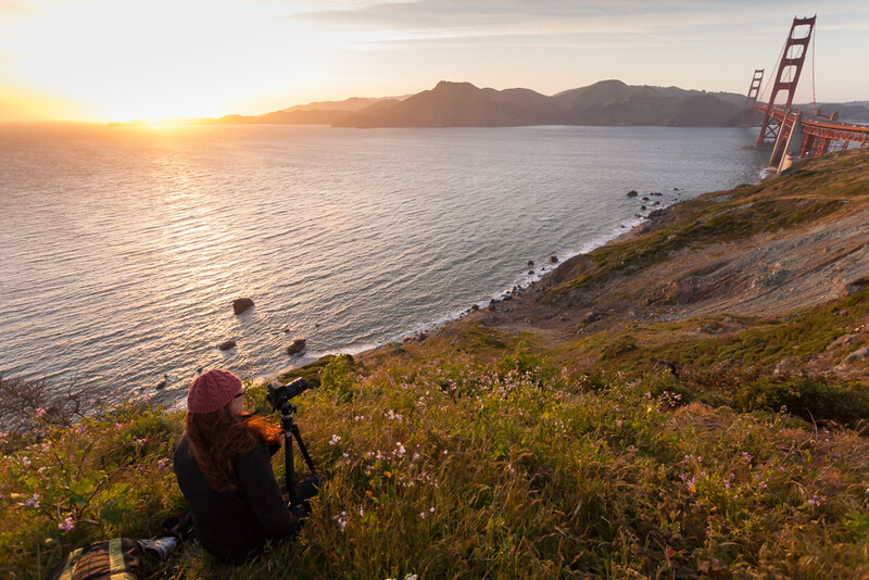 Photographer capturing sunset over bay with iconic suspension bridge visible on right horizon.