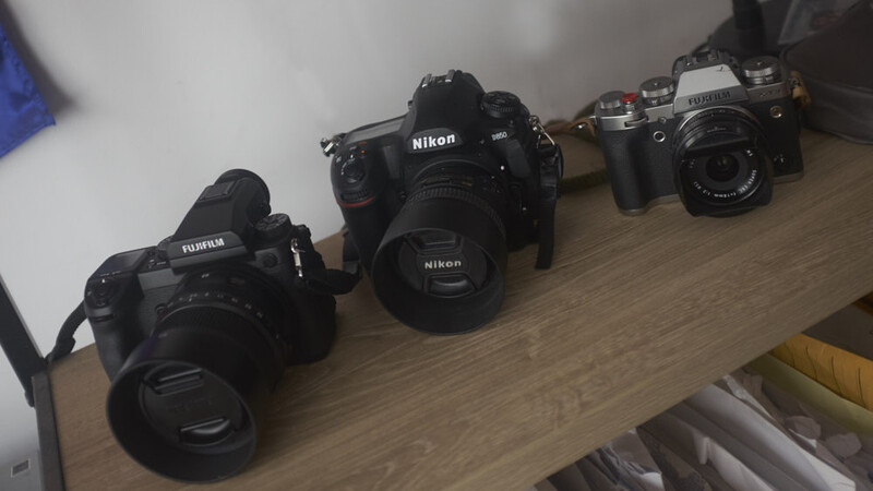 Four camera bodies arranged in a row on a wooden surface, including Fujifilm and Nikon models.