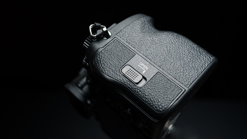 Top-down view of a professional camera body with textured grip and control buttons against black background.