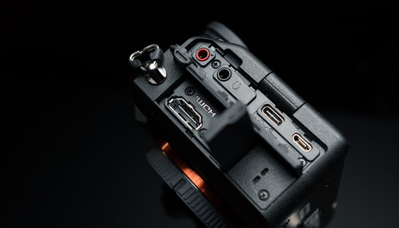 Top-down view of a professional video camera showing control buttons, knobs, and dual LCD screens against a black background.