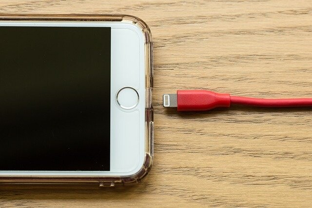 White iPhone with red Lightning cable on wooden surface next to home button.