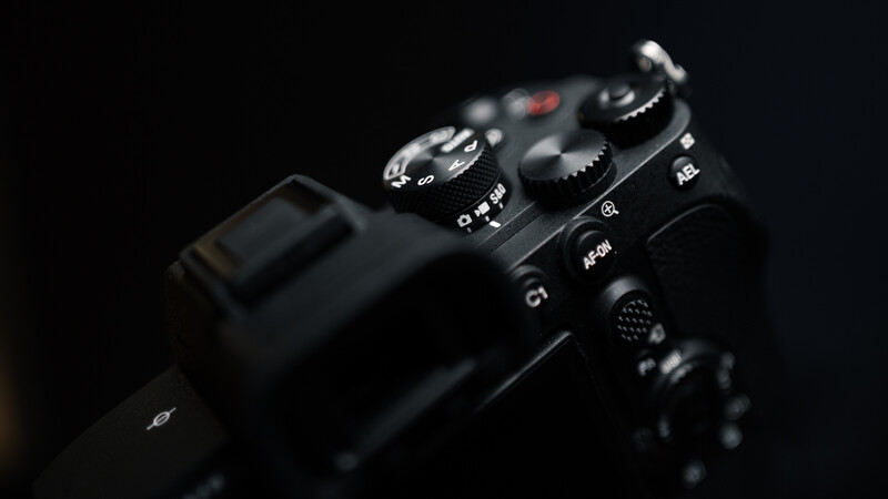 Professional camera body photographed against a black background, showing control dials and buttons in sharp detail.