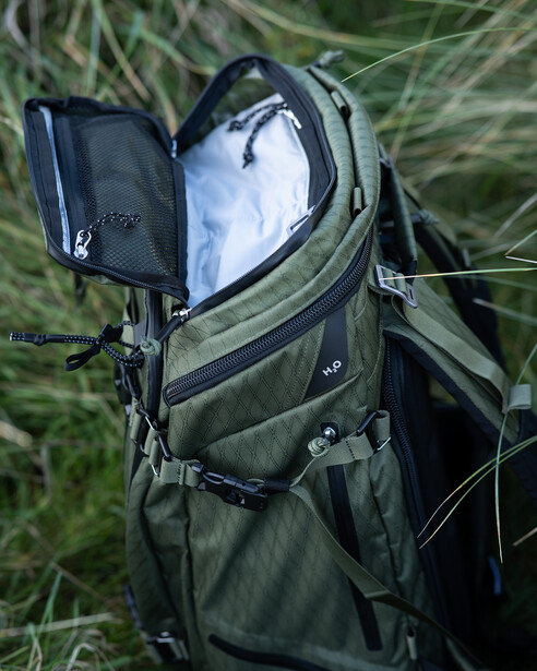 Open camera backpack displaying internal compartments and protective padding with natural grass background.