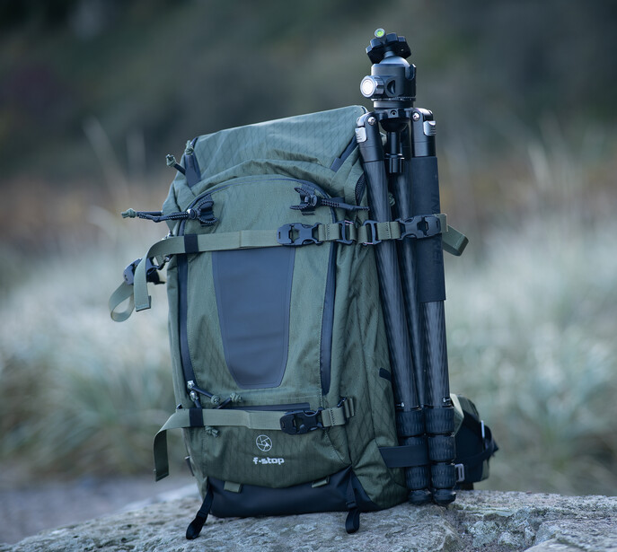 Hiking backpack with mounted bicycle secured to its frame against a misty outdoor backdrop.