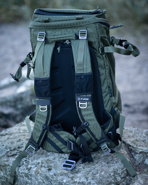Olive and navy tactical backpack displayed from behind on a gray rock, showing padded straps and multiple attachment points.