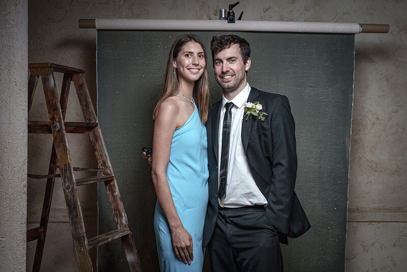 Couple in formal attire posing together against a green chalkboard backdrop with a wooden ladder visible to the left.
