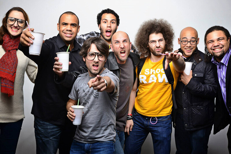Seven smiling men and women holding drinks, posing together against a white background.