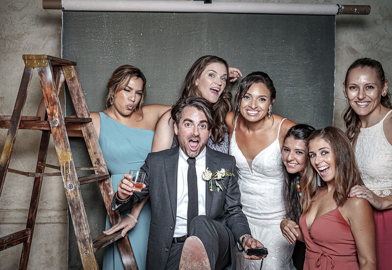 Group of eight people posing together indoors with a wooden ladder and chalkboard backdrop.