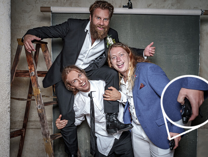 Three people posing playfully in an industrial studio setting with a ladder and blackboard visible.