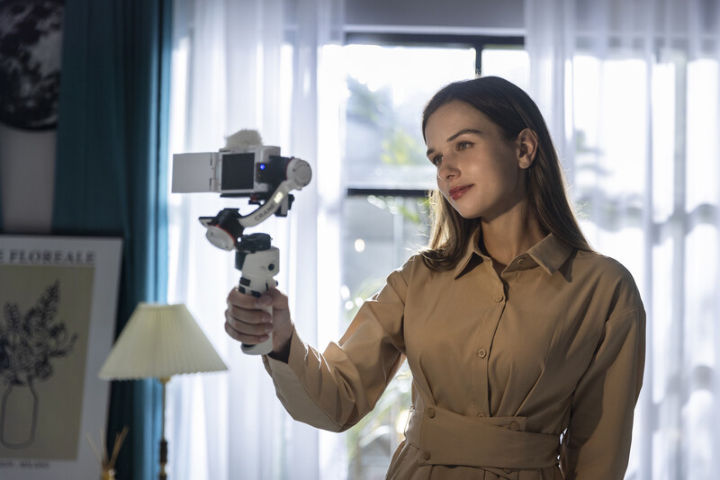 Woman holding a gimbal-mounted camera on a stabilizer rig indoors.