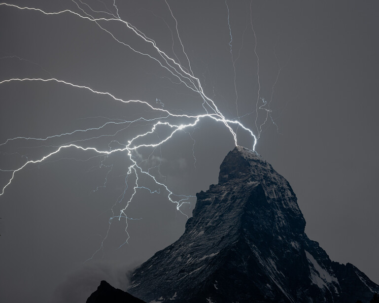 Lightning bolts strike the peak of a jagged mountain during a severe thunderstorm.