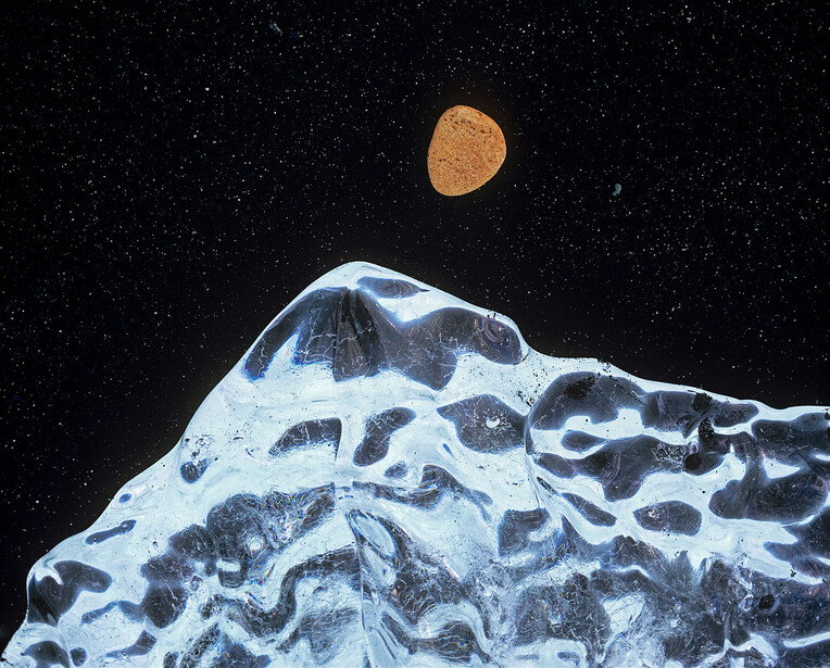 Textured white surface with dark crevices against starry black space, with an orange celestial body above.