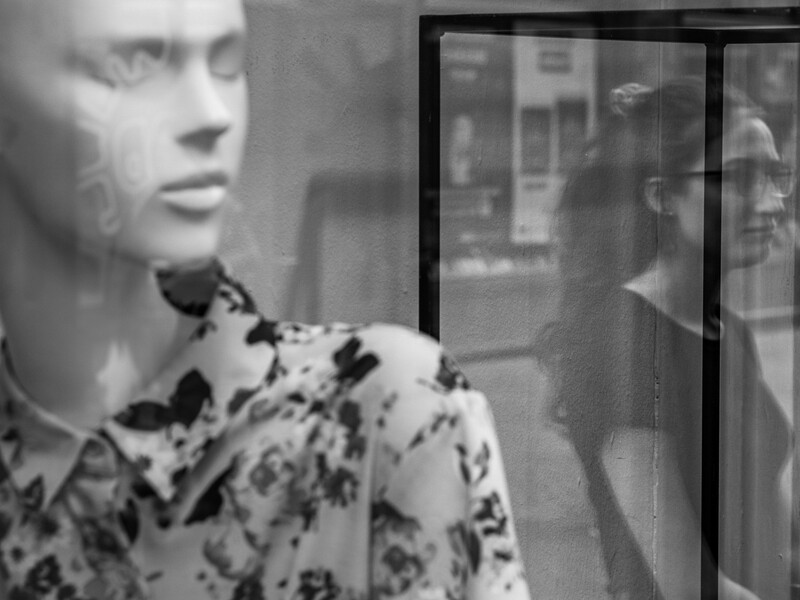 Woman in patterned blouse looking toward window with reflections visible in glass panes.