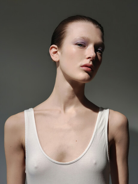Woman in white tank top photographed against neutral gray background in three-quarter view.