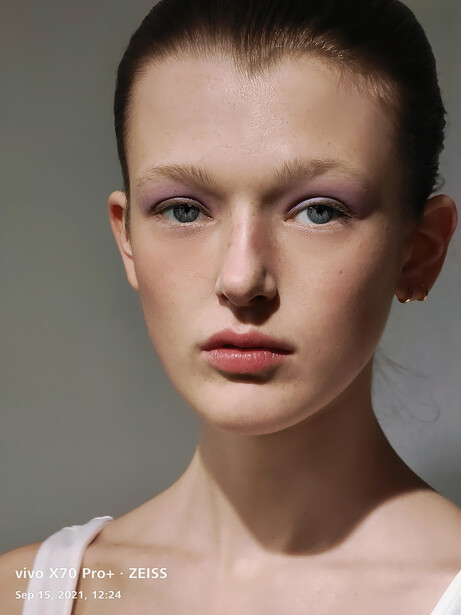 Portrait of a young woman with slicked-back hair against a neutral gray background.