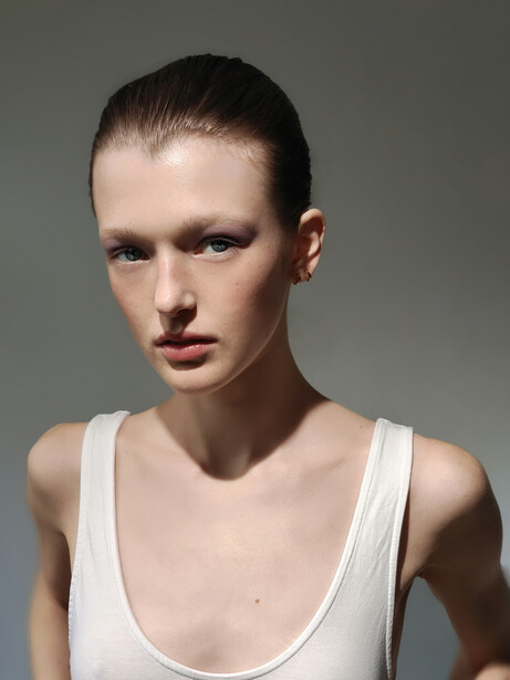 Portrait of a person with short dark hair wearing a white sleeveless tank top against a neutral gray background.