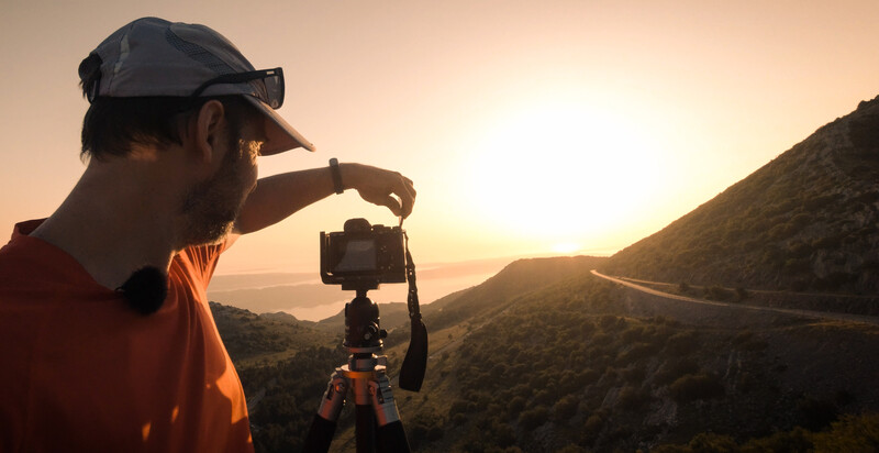 Filmmaker adjusting a smartphone mounted on a tripod while capturing sunset landscape footage in a mountainous valley.