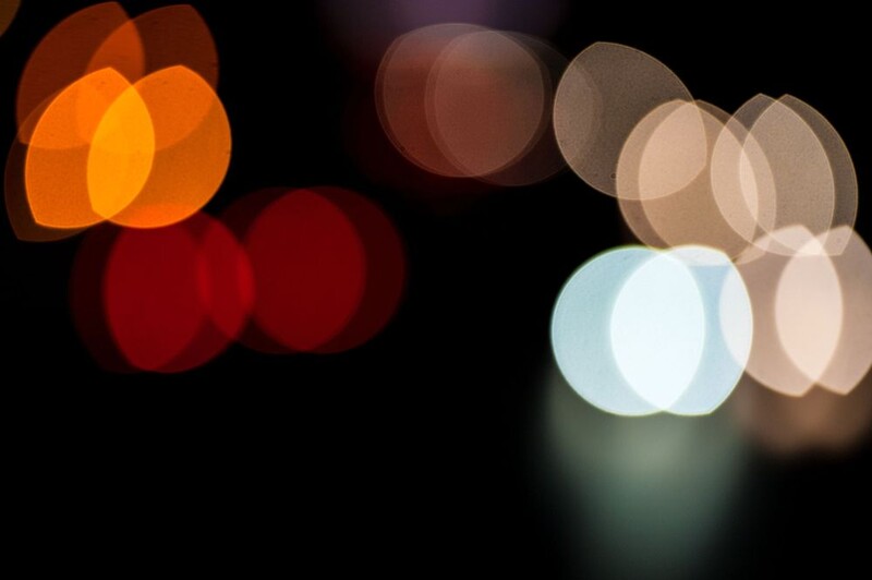 Blurred bokeh lights in orange, red, and warm white tones against a dark background.