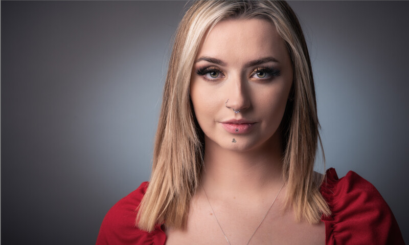 Woman with shoulder-length blonde hair wearing a red top, posed against a neutral gray background.