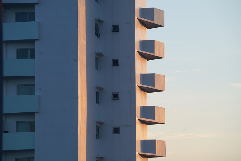 Modern residential building with stacked rectangular balconies casting shadows in golden hour light.