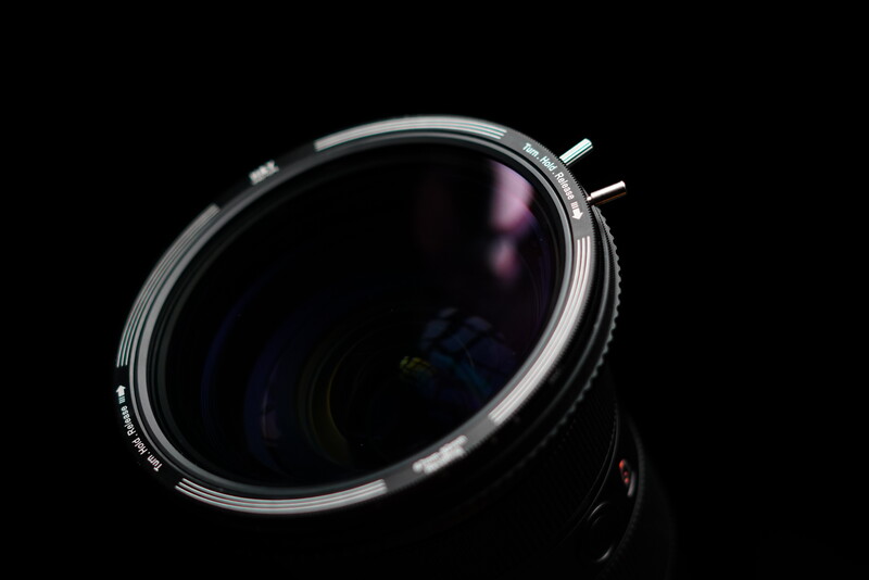 Vintage camera lens with dark glass and metal adjustment rings against black background.