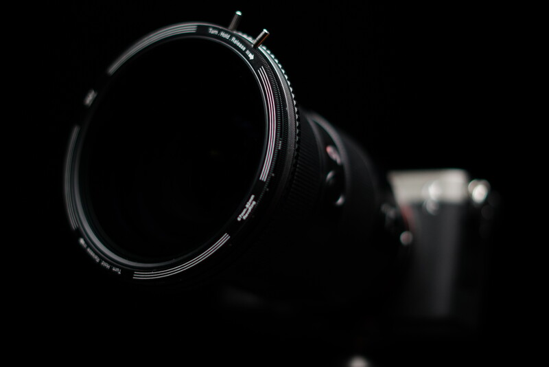 Filter ring attachment mounted on camera lens against dark background with blurred camera body in background.