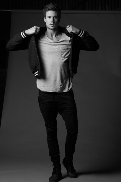 Male model in casual outfit with jacket over shoulder against neutral background.