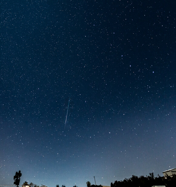 Silhouettes of people standing beneath a starry night sky with a visible meteor streak.