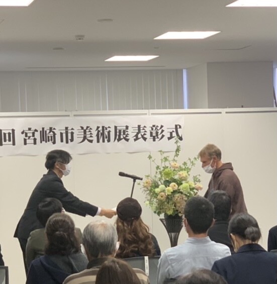 Two people shaking hands at a formal presentation event with an audience seated in foreground.