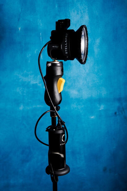 Professional studio light with fresnel lens mounted on adjustable stand against blue backdrop.